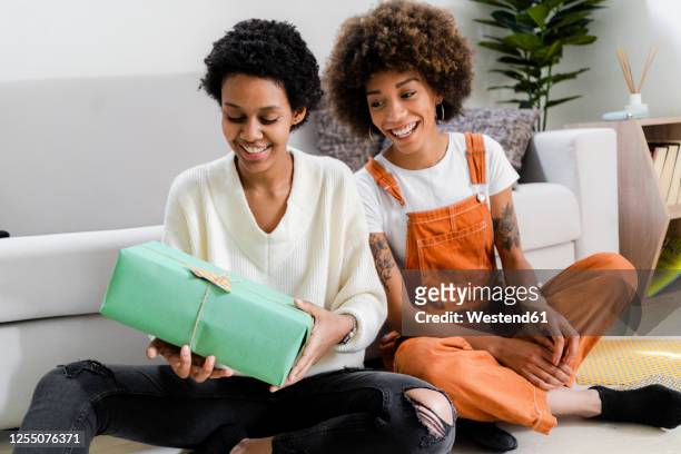 portrait of two friends sitting on the floor at home looking at gift - gift lounge stock-fotos und bilder