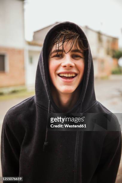 happy teenage boy wearing black hooded sweatshirt outdoors - wet sweatshirt foto e immagini stock
