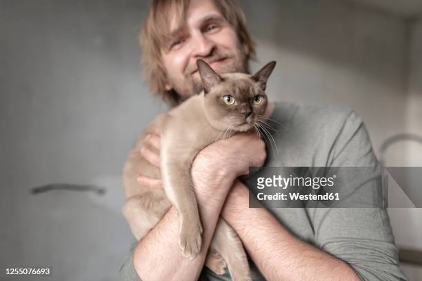 happy man carrying burmese cat during home renovation - burmese cat stock pictures, royalty-free photos & images