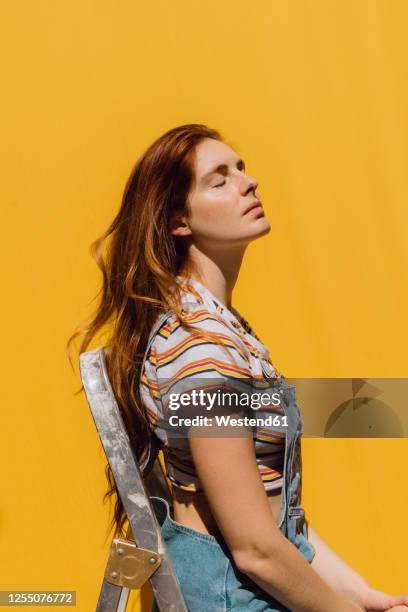 relaxed young woman sitting on ladder against yellow wall - hoofd achteroven stockfoto's en -beelden