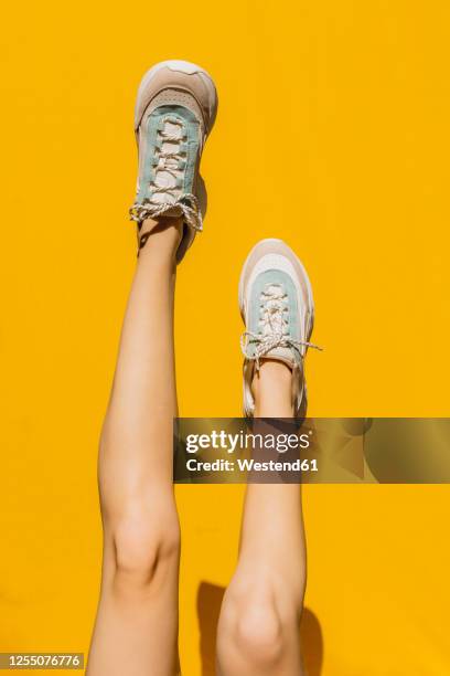 woman's legs in sports shoes over yellow wall during sunny day - knee stock pictures, royalty-free photos & images