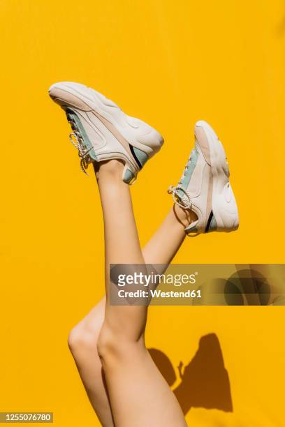 woman's legs in sports shoes over yellow wall during sunny day - woman legs stockfoto's en -beelden