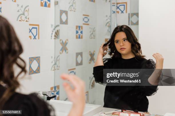 beautiful young woman with down syndrome making hair in front of bathroom mirror at home - girl looking down stock pictures, royalty-free photos & images