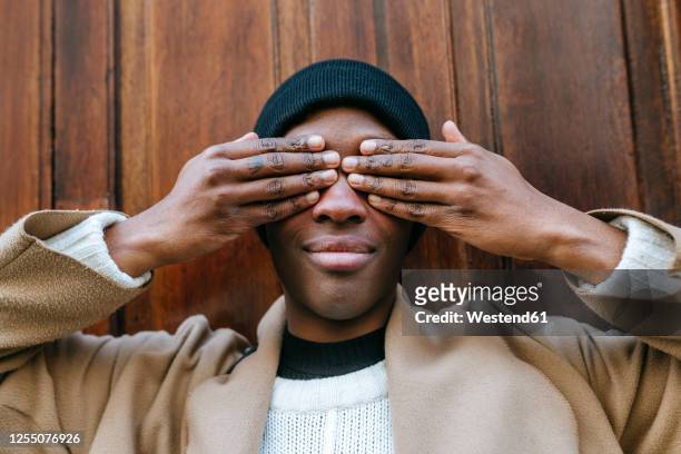 young woman covering eyes with hands against wooden wall - mani sugli occhi foto e immagini stock