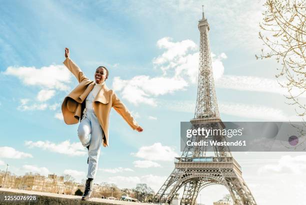 excited woman jumping from retaining wall with eiffel tower in background, paris, france - eiffeltoren stockfoto's en -beelden