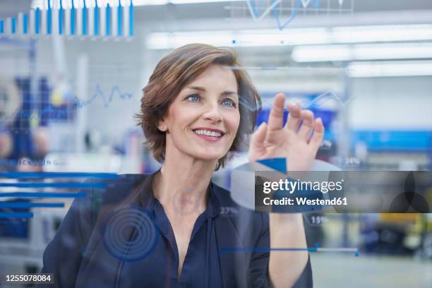 happy female manager touching line graph on glass in industry - assessment graph stock-fotos und bilder