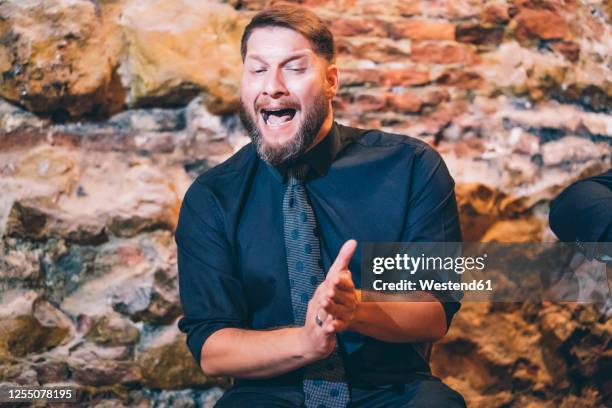 bearded singer clapping hands while singing against wall in club - flamenco 個照片及圖片檔