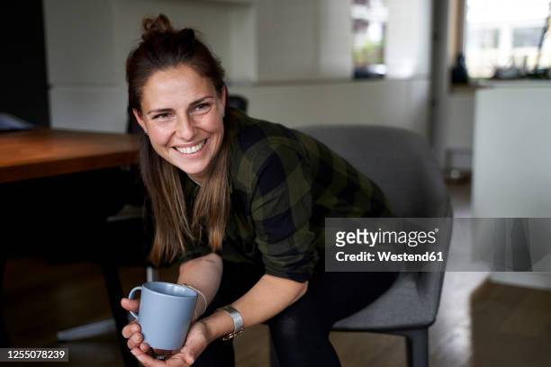 smiling woman holding coffee mug looking away while sitting on chair at home - 35 39 anni foto e immagini stock