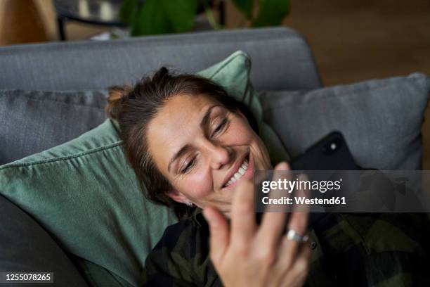 close-up of smiling woman watching video over smart phone relaxing on sofa at home - watching video stock-fotos und bilder