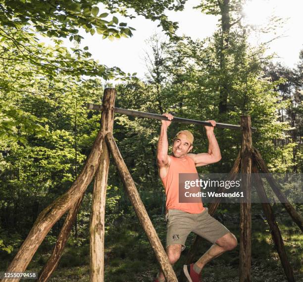 mature man doing chin-ups on horizontal bar against trees at park - horizontal bar stock pictures, royalty-free photos & images