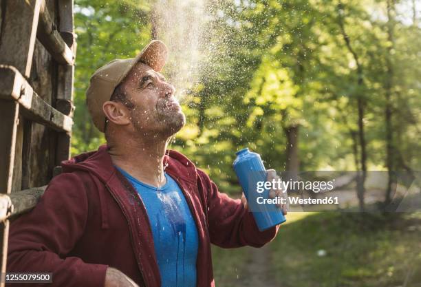 mature man spitting water while standing against wooden ladder at park - spit stock pictures, royalty-free photos & images