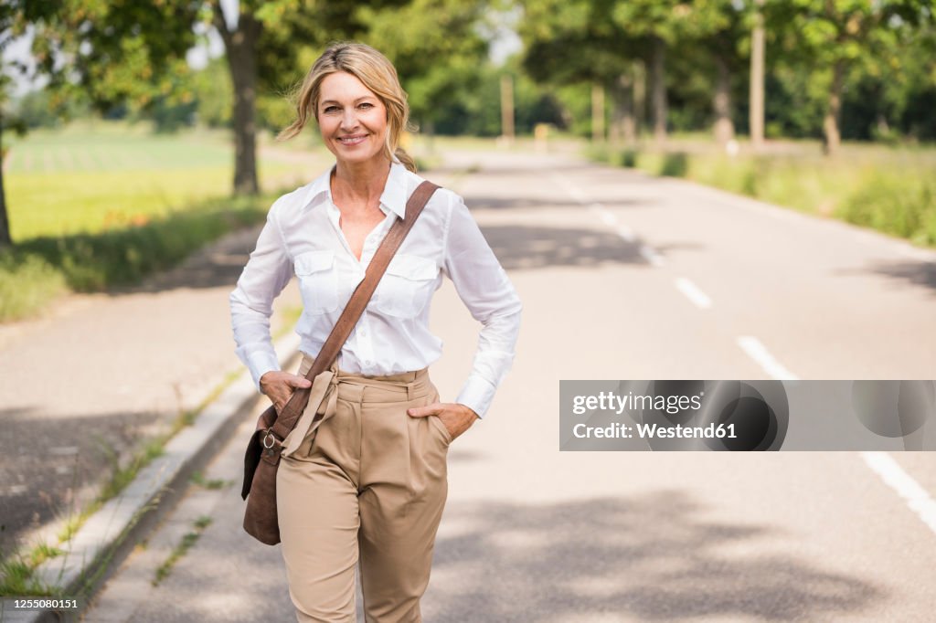 Confident mature businesswoman carrying shoulder bag while walking on road