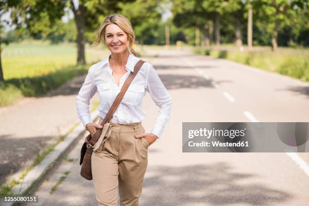 confident mature businesswoman carrying shoulder bag while walking on road - shoulder bag stock pictures, royalty-free photos & images