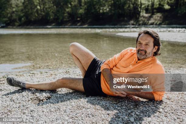 thoughtful mature man lying at riverside during sunny day - lying on side stock-fotos und bilder