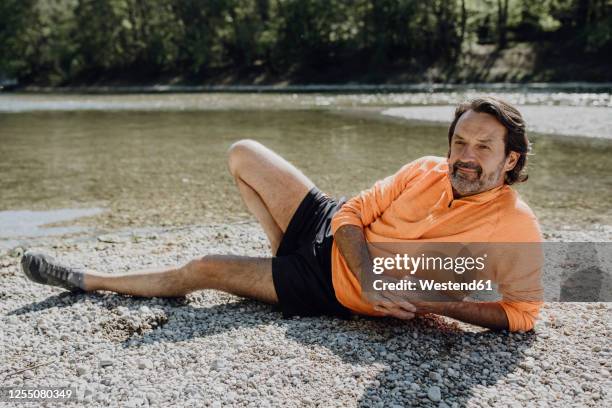 thoughtful mature man lying at riverside during sunny day - acostado de lado fotografías e imágenes de stock