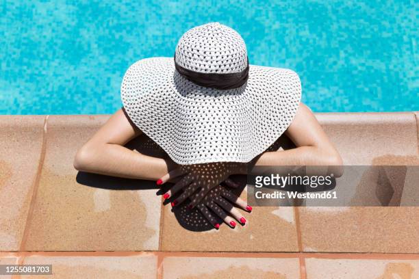 young woman wearing hat relaxing at poolside during sunny day - swimming pool and hand stock-fotos und bilder