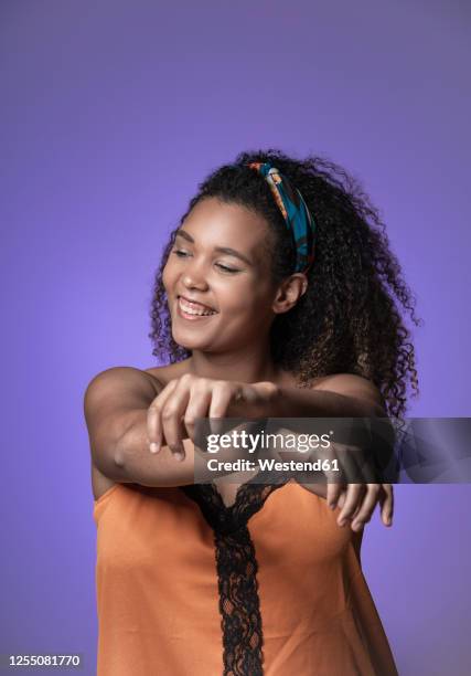 cheerful young woman with curly hair dancing against purple background - purple bandanna stock pictures, royalty-free photos & images