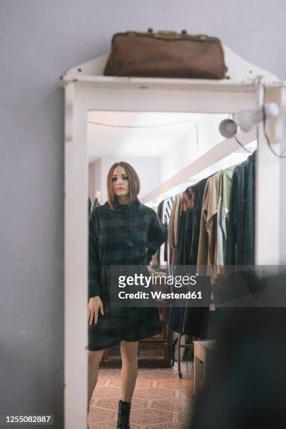 young woman trying dress looking in mirror at design studio - anprobekabine stock-fotos und bilder