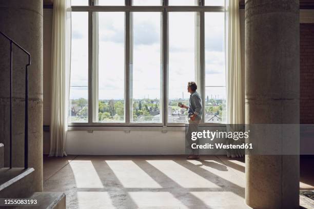 senior man looking out of window in a loft flat - loft interior foto e immagini stock