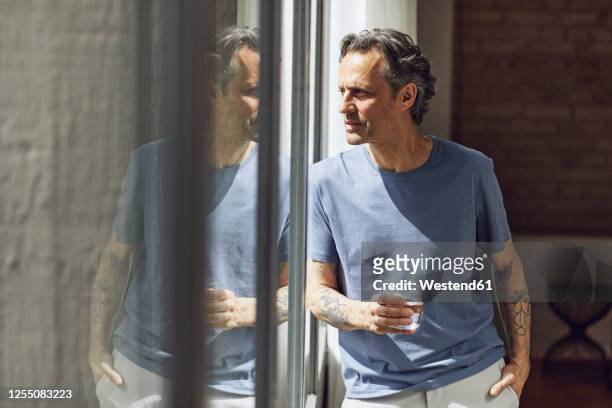 senior man looking out of window in a loft flat - mineral water stock pictures, royalty-free photos & images