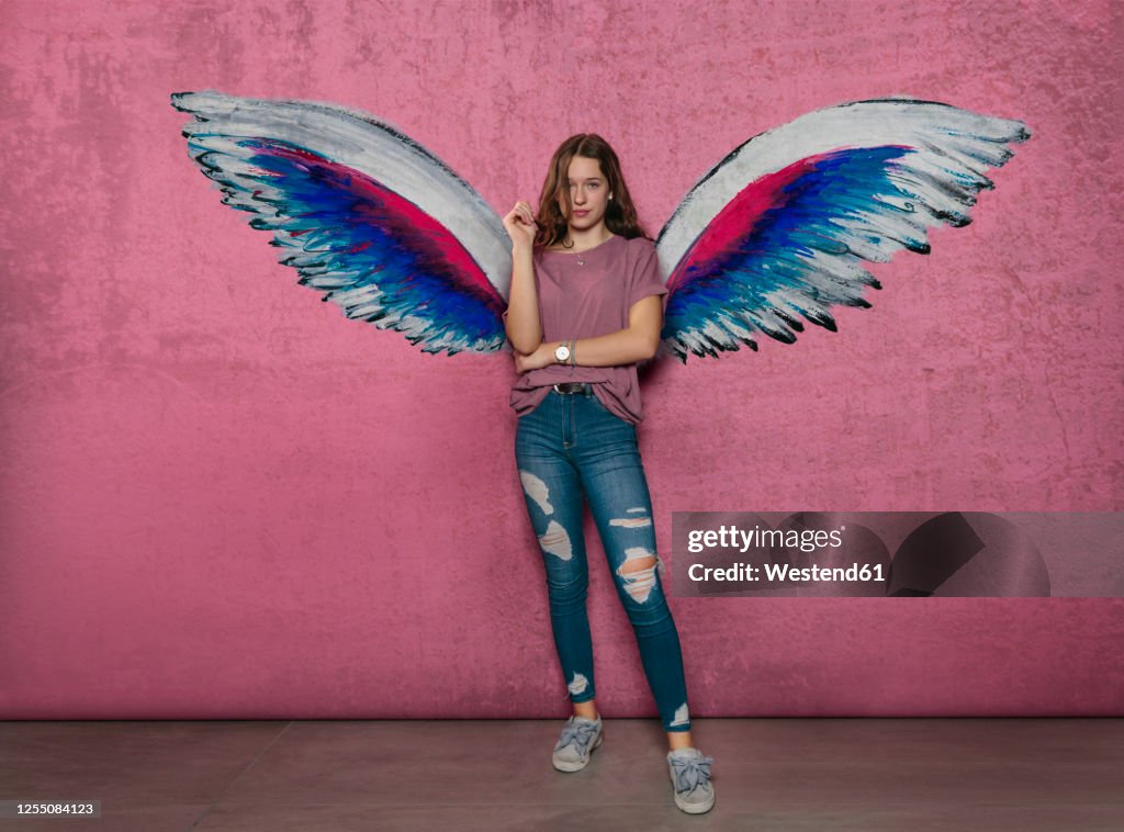 Teenage girl standing against angel wings graffiti on pink wall