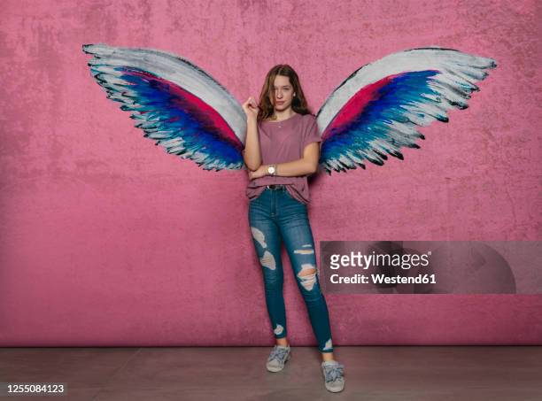 teenage girl standing against angel wings graffiti on pink wall - tierflügel stock-fotos und bilder