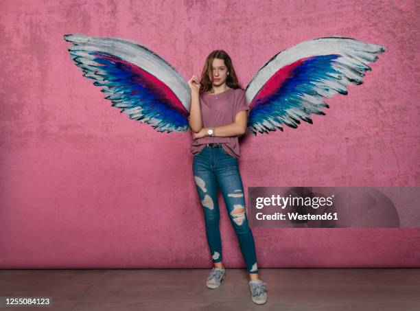 teenage girl standing against angel wings graffiti on pink wall - 羽 ストックフォトと画像