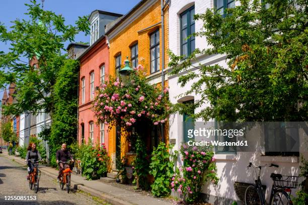 denmark, copenhagen, man and woman riding bicycles along street of historical nyboder district - copenhagen stock-fotos und bilder