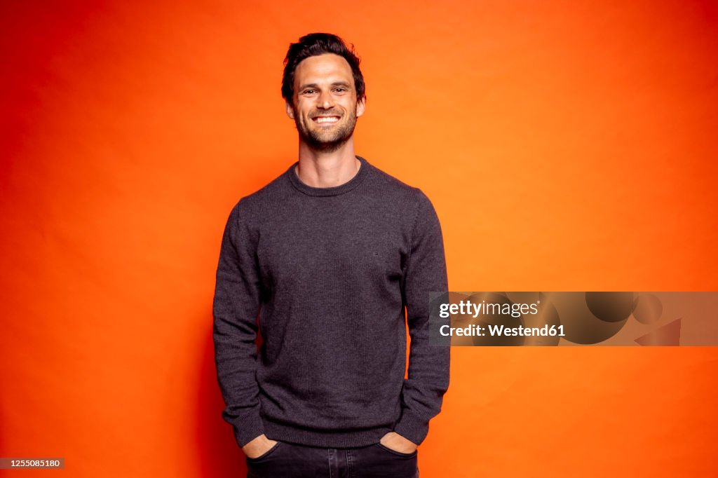 Happy handsome man with hands in pockets against orange background