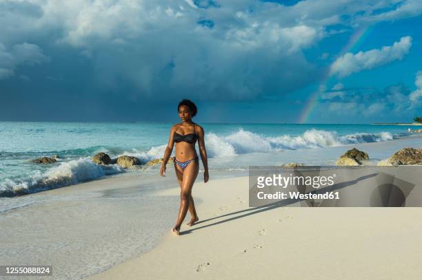 woman wearing bikini walking at grace bay beach against cloudy sky, providenciales, turks and caicos islands - providenciales stockfoto's en -beelden