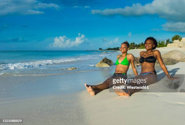 smiling female friends wearing bikinis relaxing at grace bay beach during sunset, providenciales, turks and caicos islands - grand bahama stock pictures, royalty-free photos & images