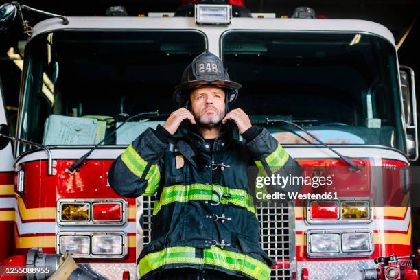 usa, new york,portrait of firefighter putting on helmet in front of fire engine - firefighter stock pictures, royalty-free photos & images