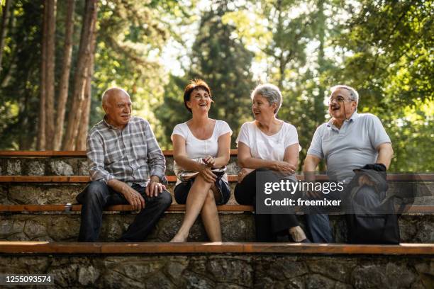 två äldre par sitter i parken, tar en paus från promenader - bench park bildbanksfoton och bilder