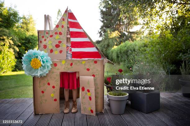 child (6-7) playfully pulling a silly face through the gaps inside a homemade playhouse made from recycled cardboard - playhouse stockfoto's en -beelden