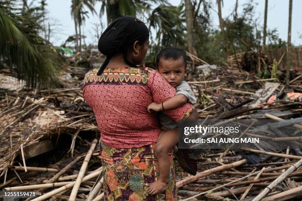 Rohingya woman carries her baby next to her destroyed house at Basara refugee camp in Sittwe on May 16 after cyclone Mocha made a landfall. The death...