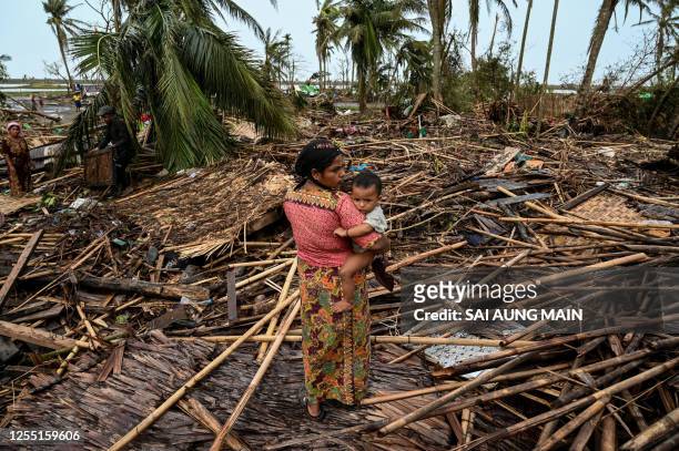 Rohingya woman carries her baby next to her destroyed house at Basara refugee camp in Sittwe on May 16 after cyclone Mocha made a landfall. The death...