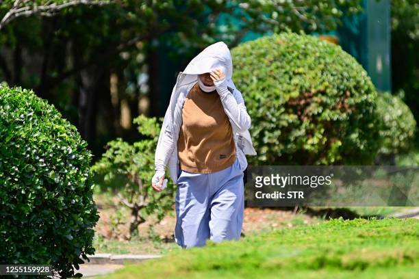 Woman walks with a clothing as a sun shade amid hot weather in Qingzhou, in China's eastern Shandong province on May 16, 2023. / China OUT