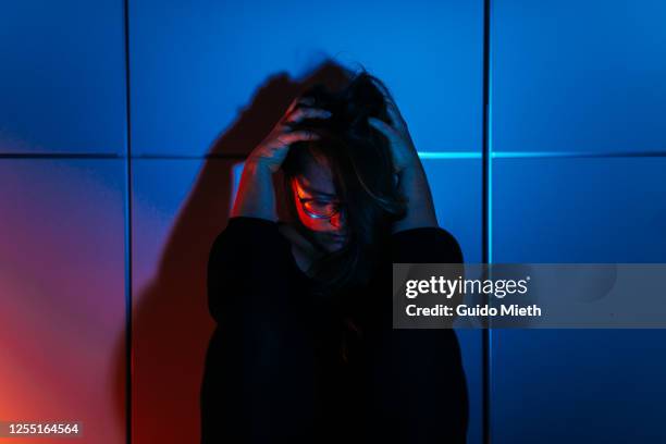 sad woman sitting in front of cabinet in the dark. - schizofrenie stockfoto's en -beelden