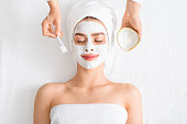 Spa therapist putting facial mask for young lady