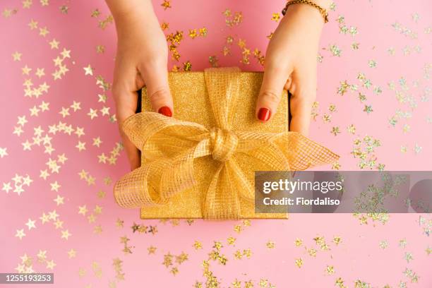 hands of woman holding a green gift box with a yellow satin ribbon on pink background - wedding gift stock pictures, royalty-free photos & images