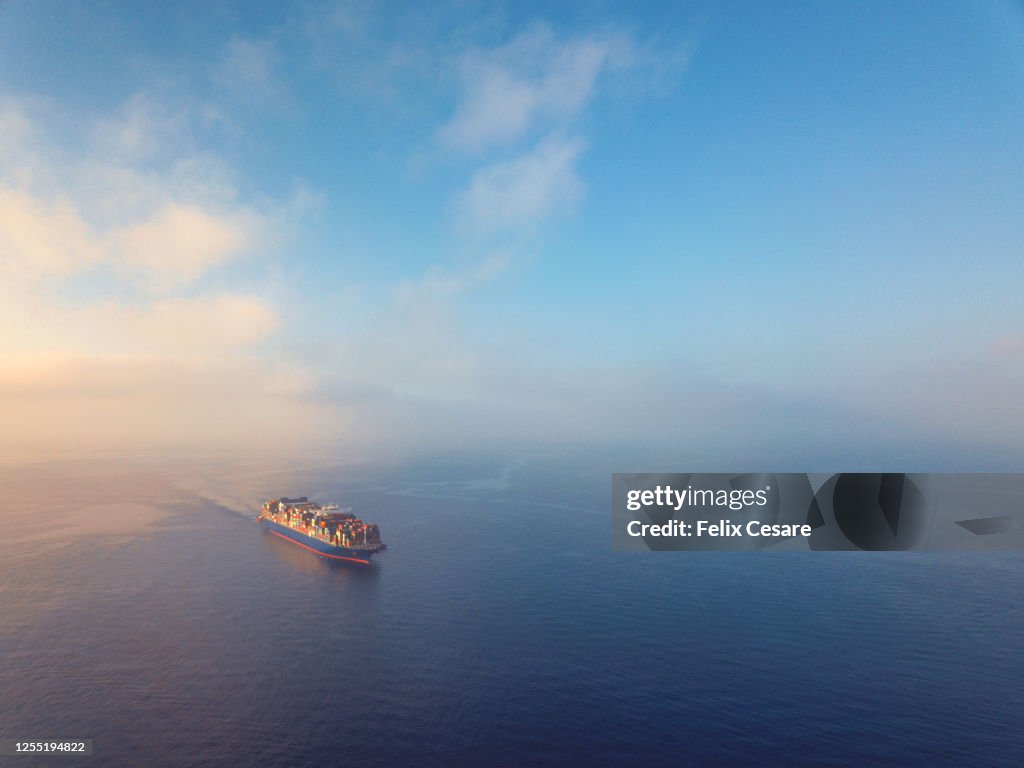 Aerial view of a solo cargo ship on the move in open waters during sunrise.
