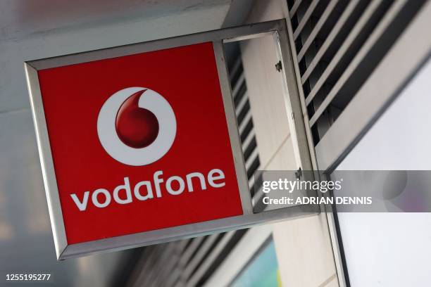 Vodafone logo is pictured on a sign above a store in central London on May 16, 2023. British mobile giant Vodafone is to axe 11,000 jobs over three...