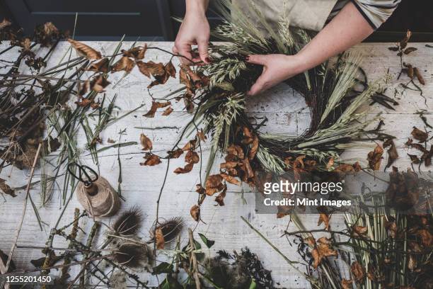 woman making a small winter wreath of dried plants, brown leaves and twigs, and seedheads. - wreath making stock pictures, royalty-free photos & images