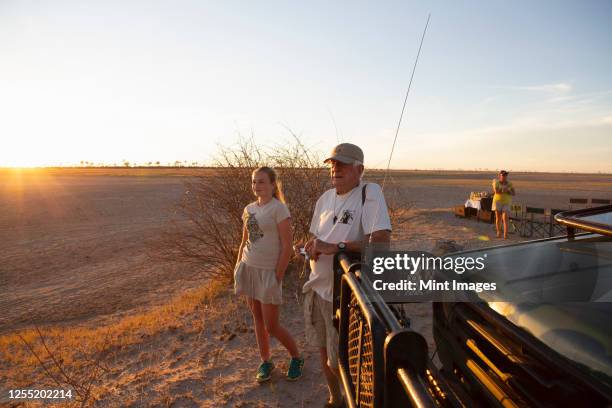 a grandfather and his grand daughter looking out at sunset in the kalahari desert - kalahari stock-fotos und bilder