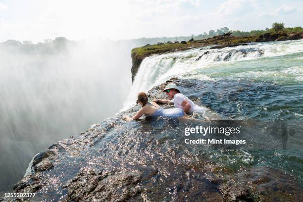 man and a girl, father and daughter in the water of the devil's pool on the edge of victoria falls, mist rising from the falling water. - zambia foto e immagini stock