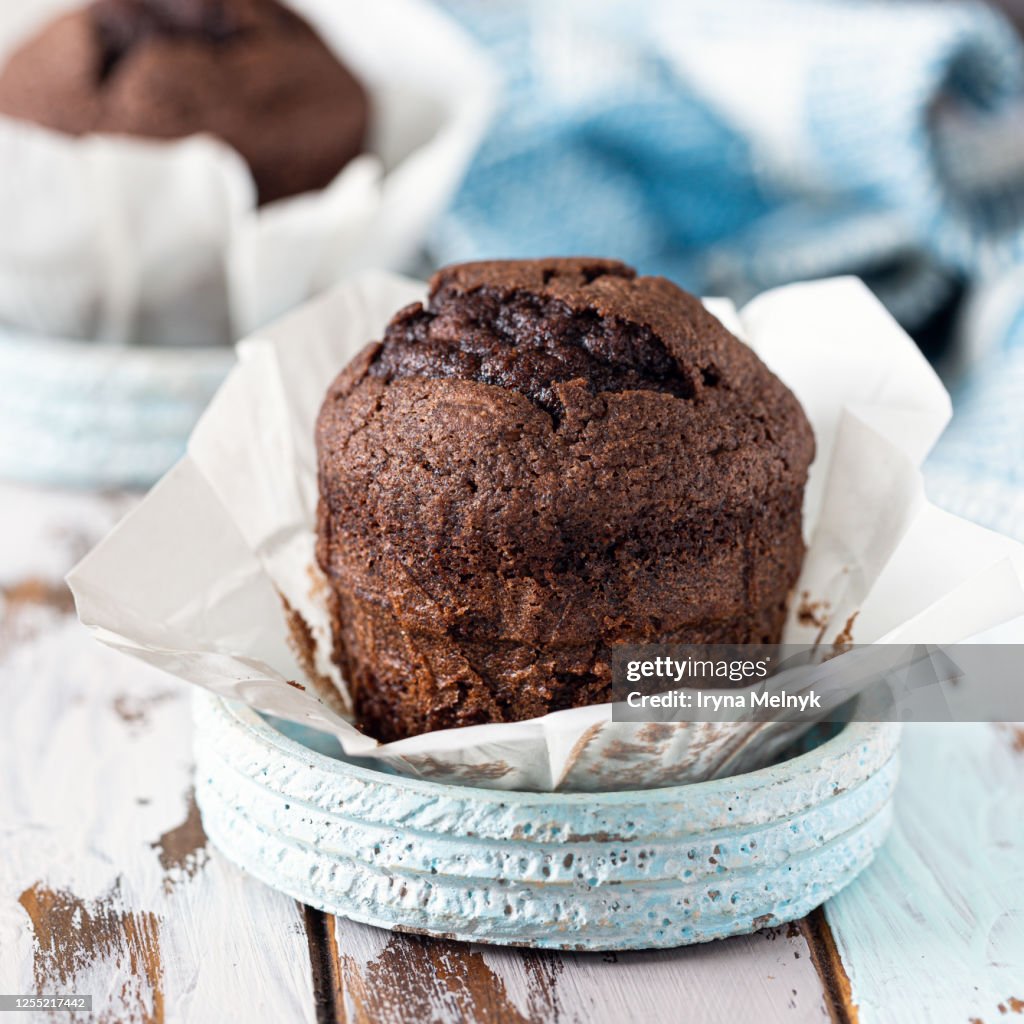 Delicious homemade chocolate muffin on an old rustic wooden table with a blue knitted napkin