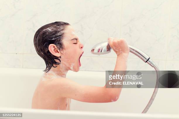 boy sitting in bath singing into a shower head - boy taking a shower stock-fotos und bilder