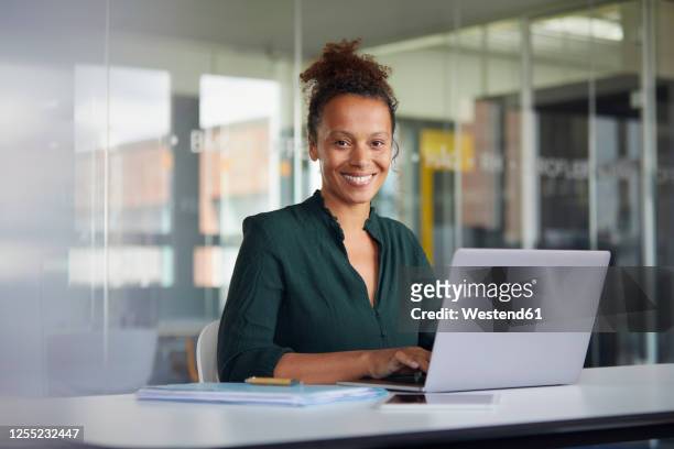 portrait of smiling businesswoman working on laptop at desk - stralende lach stockfoto's en -beelden