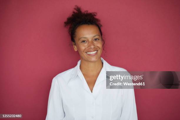 portrait of smiling businesswoman against red background - portrait femme fond rouge adulte photos et images de collection