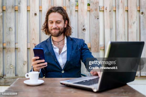 businessman smirking while using mobile phone sitting at cafe - sourire narquois photos et images de collection